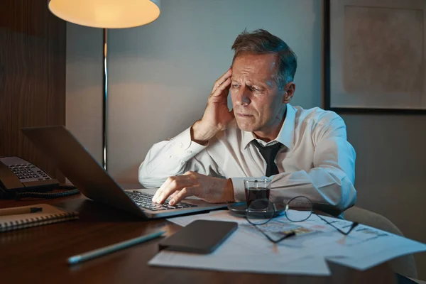 Mature businessman working overtime on laptop in hotel room — 图库照片