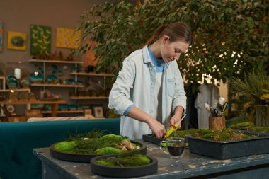 Gülümseyen bayan yeşil bitkilerle resim yapıyor.