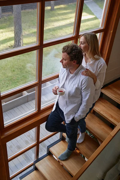 Tender woman standing behind her husband near window — Stock Photo, Image