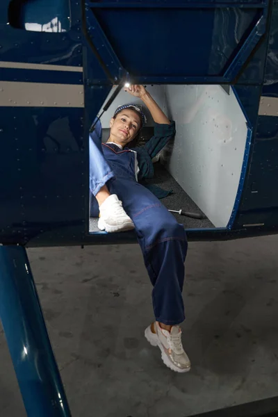 Mecânico feminino atraente deitado debaixo de um motor a jato — Fotografia de Stock