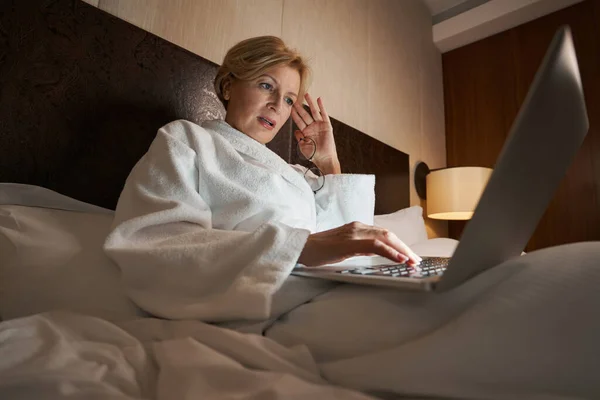 Εστιασμένη επιχειρηματίας που εργάζεται εξ αποστάσεως από άνετο κρεβάτι ξενοδοχείου — Φωτογραφία Αρχείου
