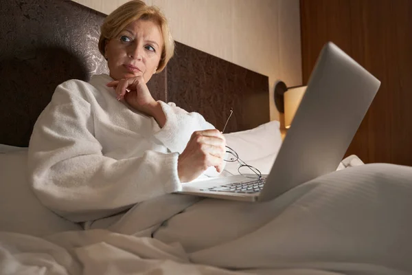 Aggódó szőke nő használja a laptopját az ágyban. — Stock Fotó
