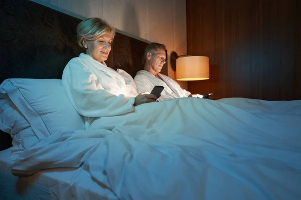 Entspanntes Paar chillt im Bett und schaut aufs Smartphone — Stockfoto