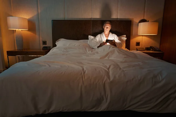 Caballero serio usando su teléfono inteligente antes de irse a dormir — Foto de Stock