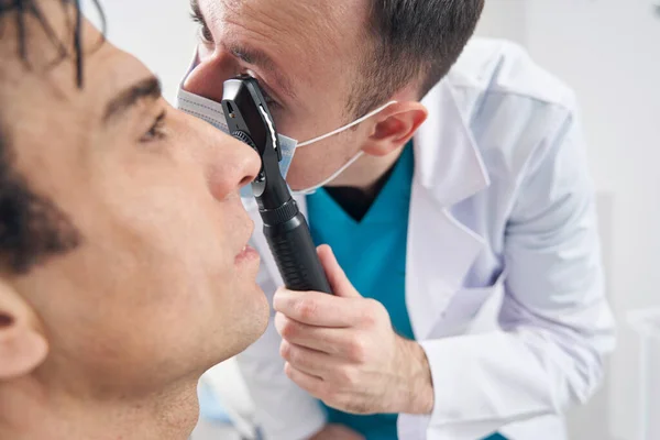 Homme médecin penché vers le patient, examine attentivement le fond des yeux — Photo