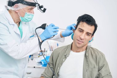 Otorhinolaryngolog hastanedeki tıbbi aletle hastayı muayene ediyor.