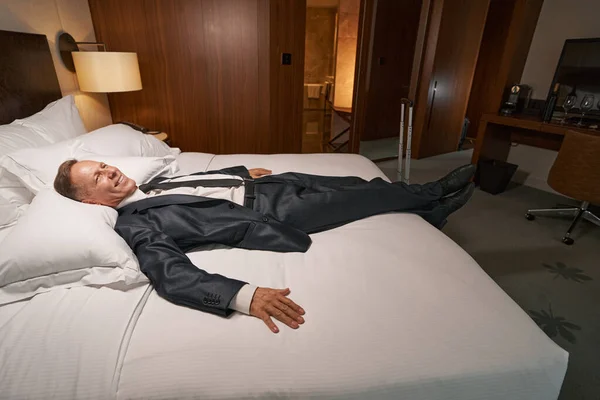 Homem de negócios relaxado em traje formal descansando na cama do hotel — Fotografia de Stock