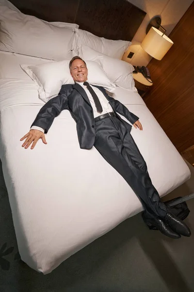 Empreendedor alegre relaxante na cama do hotel com seu terno formal em — Fotografia de Stock