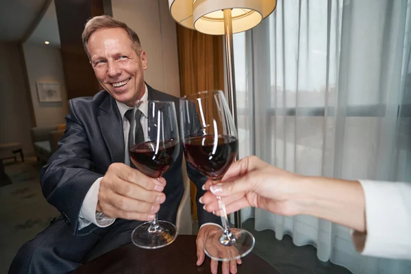Heyecanlı iş adamı mutlu hissediyor ve kırmızı şarap içiyor.