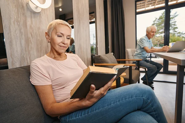 Ontspannen oudere vrouw leesboek op de bank — Stockfoto