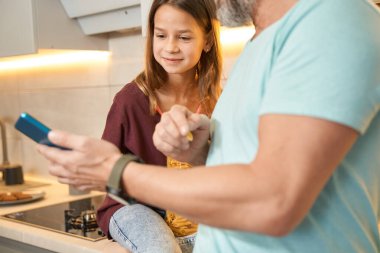 Yetişkin bir adamın elinde cep telefonunu izleyen bir genç.