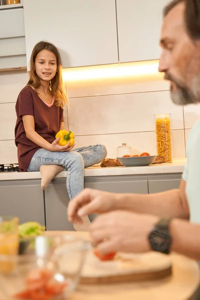 Teen ragazza è seduta mentre suo padre sta cucinando insalata — Foto Stock