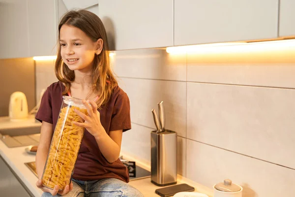 Teenager in the kitchen holding a glass container with pasta — Stock Photo, Image