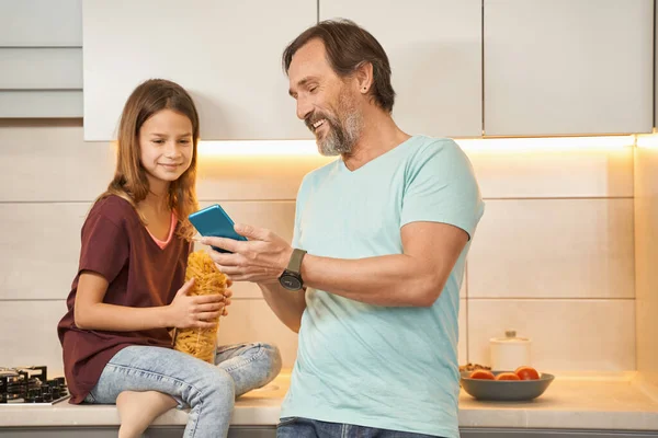 Hombre adulto con una adolescente en la cocina viendo un teléfono inteligente — Foto de Stock