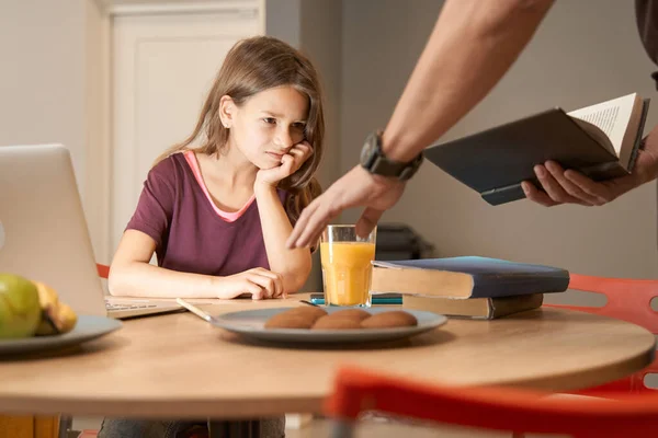Mädchen am Küchentisch betrachtet das Buch in den Händen ihrer Eltern — Stockfoto