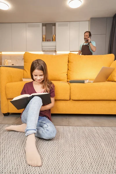 Chica leyendo libro en la sala de estar al lado de padre — Foto de Stock