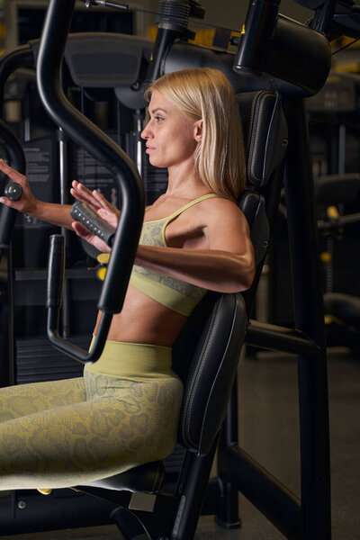 Сфокусированное фото на серьезной женщине, тренирующейся в тренажерном зале