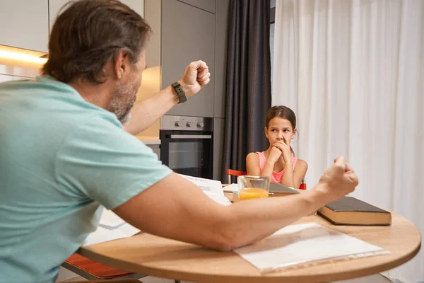 Menina sentada na mesa da cozinha na frente de um homem com raiva — Fotografia de Stock