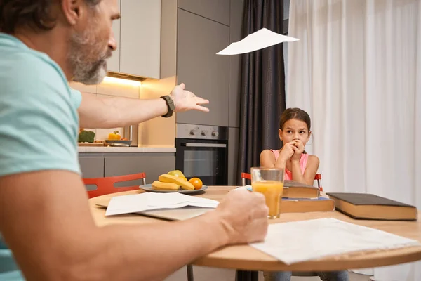 Menina sentada na mesa da cozinha com livros e documentos ao lado de homem com raiva — Fotografia de Stock
