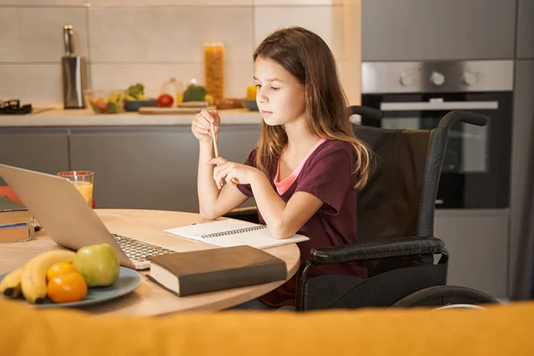 Mädchen im Rollstuhl denkt während der Hausaufgabenbetreuung am Tisch — Stockfoto