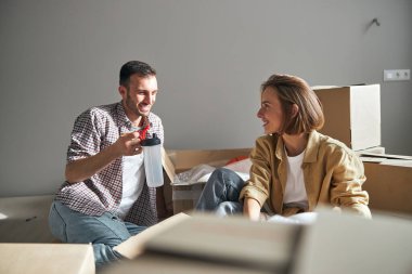 Karton kutuların arasında oturmuş gülümseyen eşler.