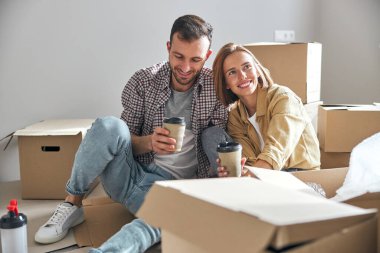 Kağıt bardakları olan gülümseyen bir çift yerde oturuyor.