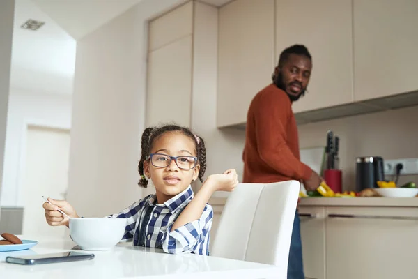 Fröhliches Mädchen isst in der Küche in Gesellschaft ihres afroamerikanischen Vaters — Stockfoto