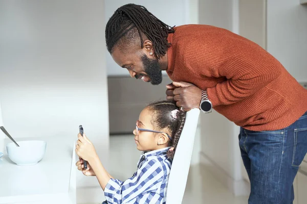 Junges Mädchen sitzt auf Stuhl und schaut mit Vater aufs Handy — Stockfoto