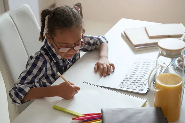 Little girl using laptop and taking notes in workbook — Stock Photo, Image