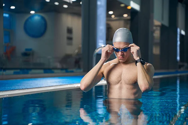 Erkek havuzda duruyor ve yüzmeye hazırlanıyor.