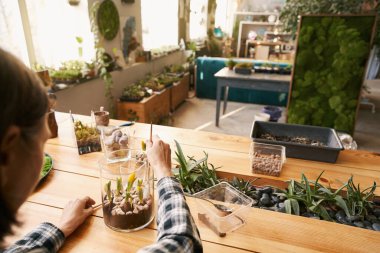 Büyük stüdyoda çalışan bir kadın, çiçek ekiyor.