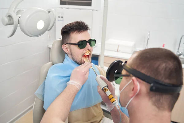 Чоловік-лікар зцілює зуб пацієнта обладнанням — стокове фото