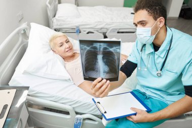Hastane yatağında yaşlı bir kadına röntgen filmi gösteriliyor.
