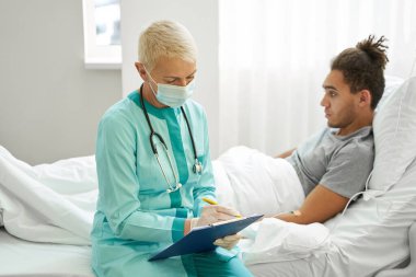 Kadın doktor, erkeğin yanında not alıyor.