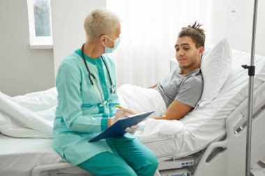 Erkek hasta doktor notlarına ilgiyle bakıyor.