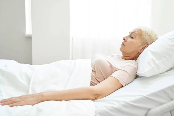 Kvinnlig pensionär vilar i sängen avdelning av vårdcentral — Stockfoto