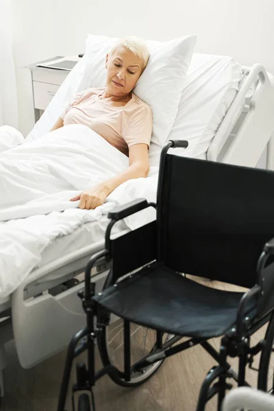 Senior citizen in bed looking at wheelchair — Stock Photo, Image