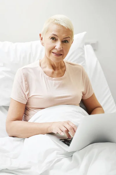Γήρας πρόσωπο κλικ στο φορητό υπολογιστή στο κρεβάτι του ιατρικού κέντρου — Φωτογραφία Αρχείου