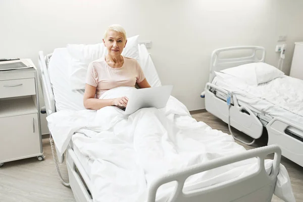 Old lady with laptop in medical bed of hospital — Zdjęcie stockowe