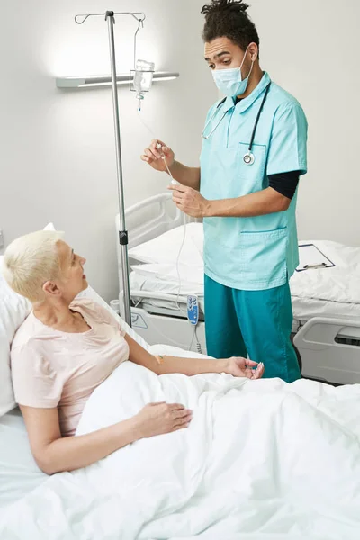 Doctor looking at pensioner while using drip chamber — Stock Photo, Image