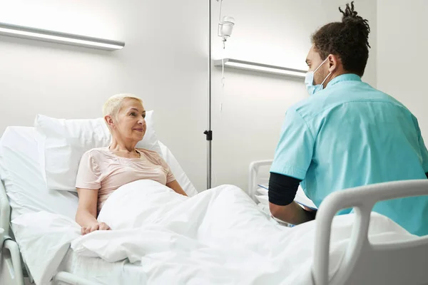 Doctor listening to old woman in hospital bed — Stock fotografie