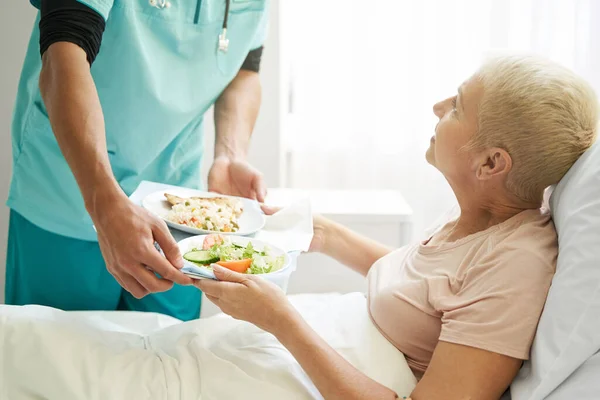 Old female taking breakfast from worker of hospital — Stock Photo, Image
