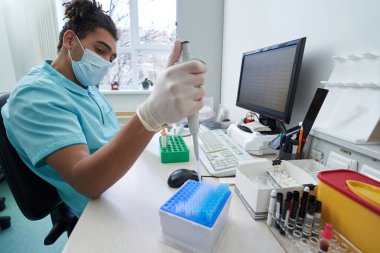 Bilgisayardan önce numunelerle çalışan genç bir erkek.