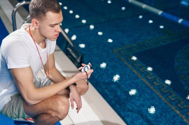 Genç beyaz adam yüzme havuzunun yakınındaki saati kontrol ediyor.