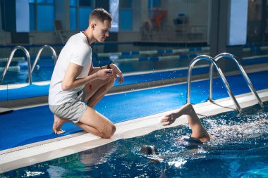 Genç adam oturmuş, yüzen bayan atleti seyrediyor.