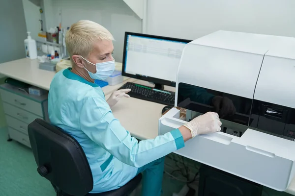 Gammal kvinna i mask arbetar med prylar på kliniken — Stockfoto