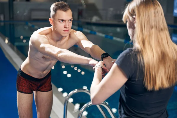 Atlética mujer tire delgada chico manos hacia sí misma antes de entrenar en la piscina — Foto de Stock