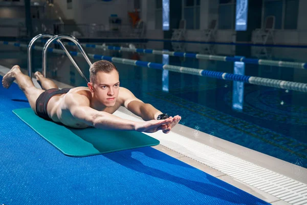 Young man doing exercises on yoga mat before training in the pool — Foto de Stock