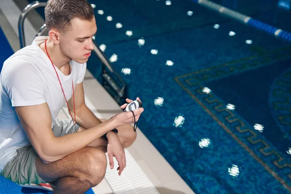 Genç beyaz adam yüzme havuzunun yakınındaki saati kontrol ediyor.