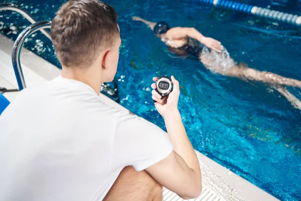 Antrenör, kadın yüzücü egzersizlerini yaparken zamanlayıcıya bakıyor.